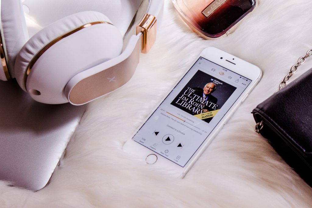 a fluffy material with a pair of headphones and a phone on top. the phone displaying an audiobook.