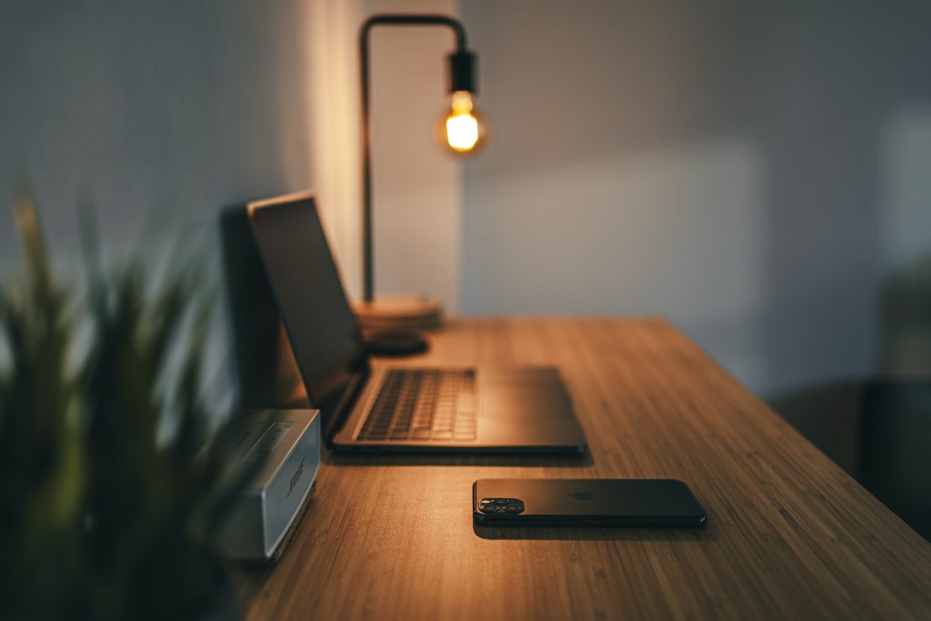 wooden desk with mood lighting, plant, laptop and phone on top.