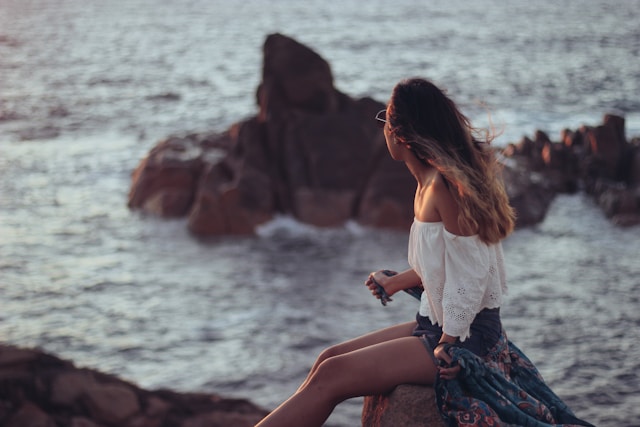 woman gazing out to sea, sat on rock at sunset